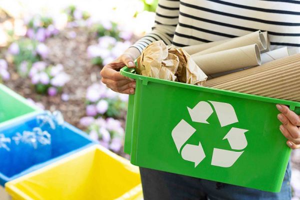 Persona llevando un contenedor verde de reciclaje con papel y cartón